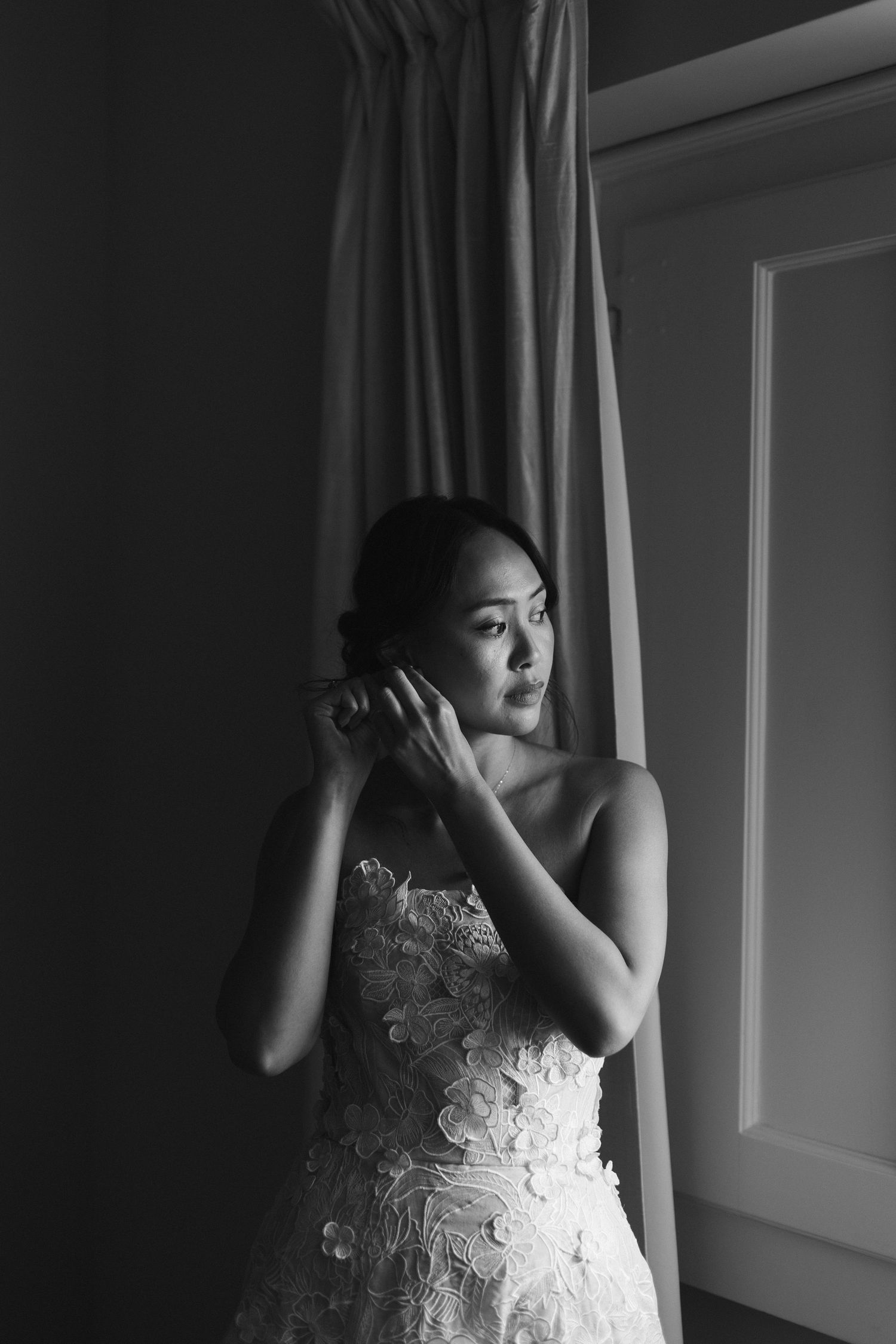 Dramatic black and white portrait of a person in a lace dress by a window.