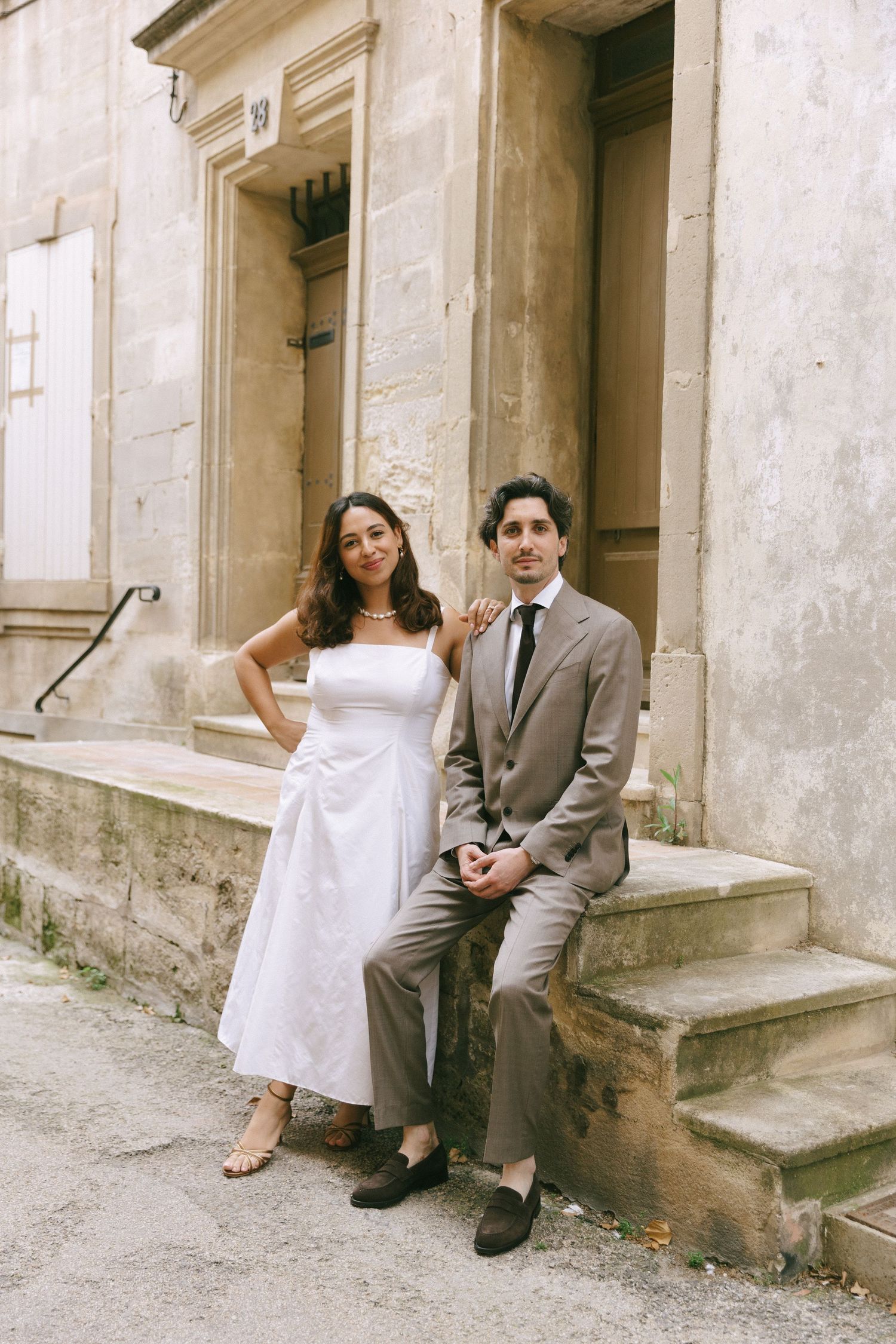 A couple in wedding attire sitting on stone steps of a classical building.