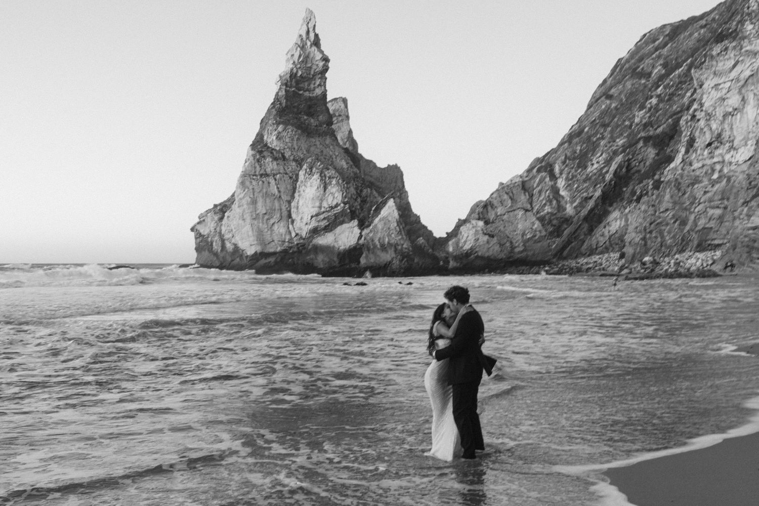 A romantic coastal photoshoot with dramatic cliffs and ocean waves in the background.