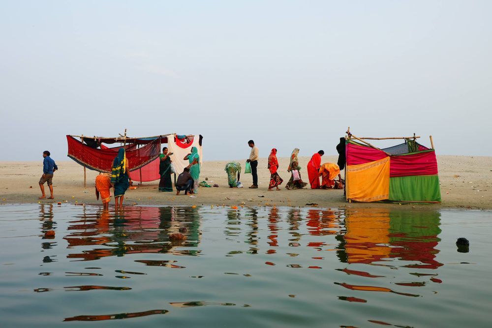 People gathered around colorful kayaks and canoes in shallow water.