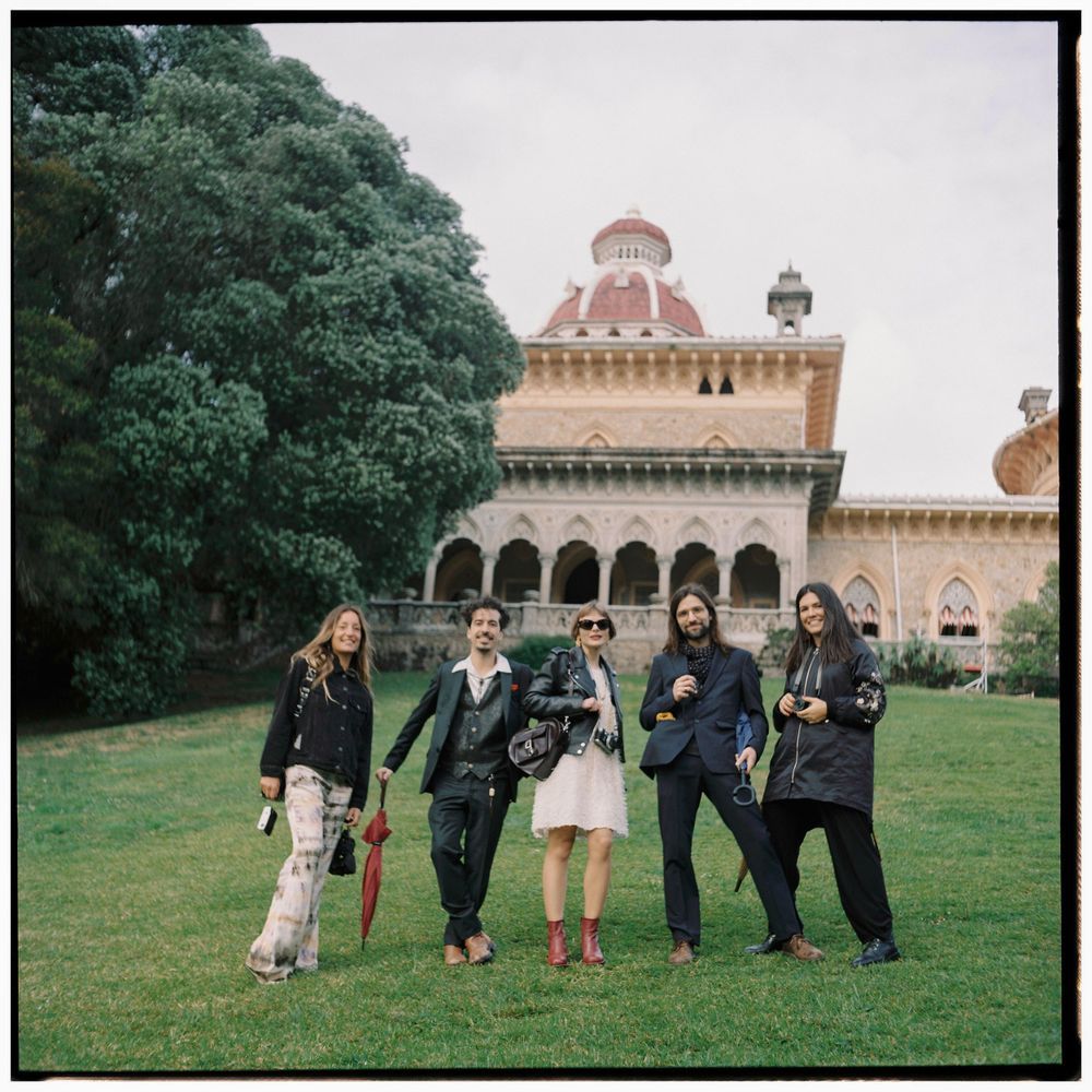 Group walking together on grassy lawn near historic castle-like building with arched windows.