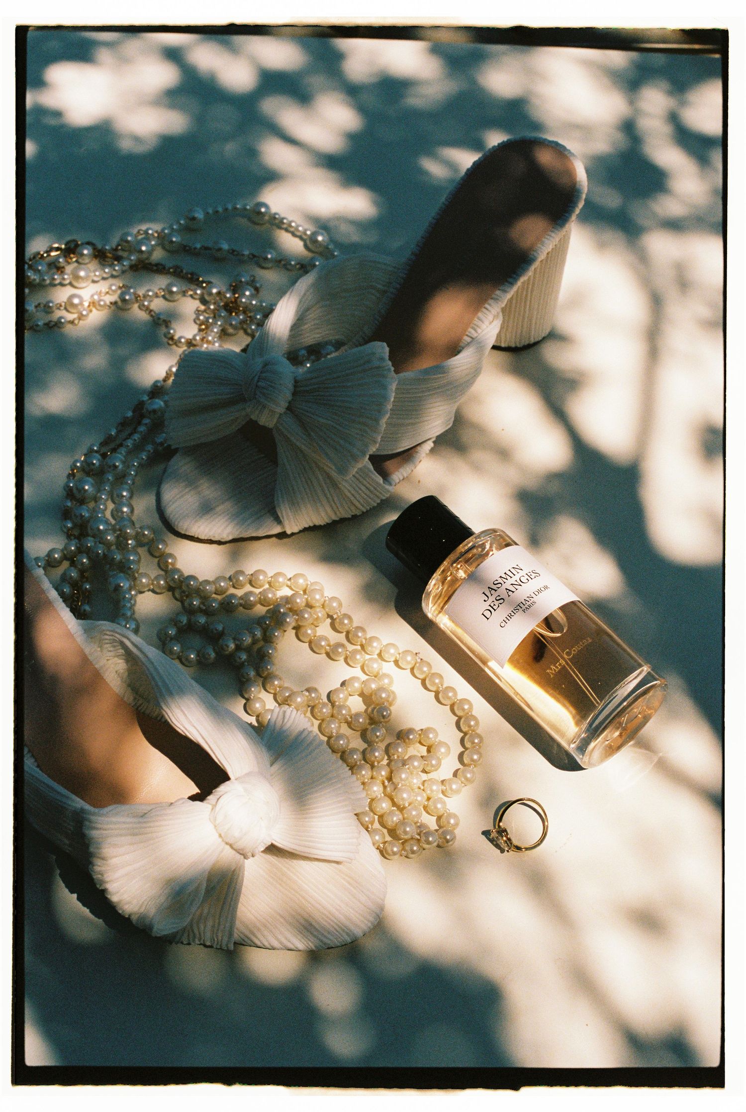 Elegant perfume bottle and pearl necklace arrangement in dappled sunlight.