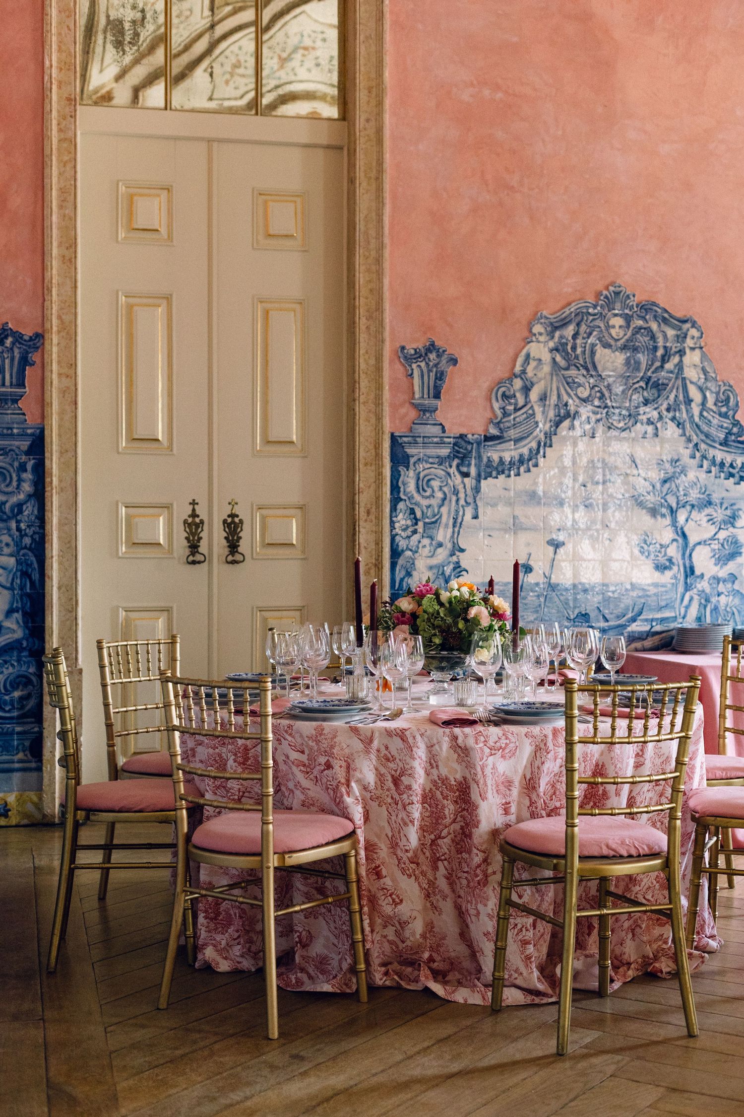 Elegant dining room with blue tile walls and pink tablecloths set for a formal event.