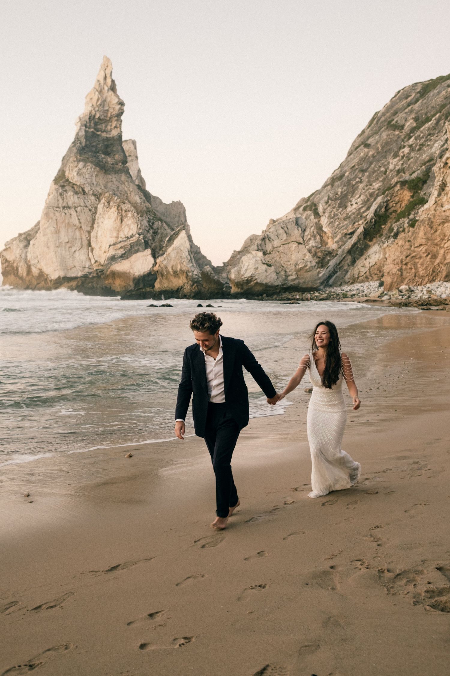 Romantic beach photoshoot with dramatic coastal rock formations at sunset.