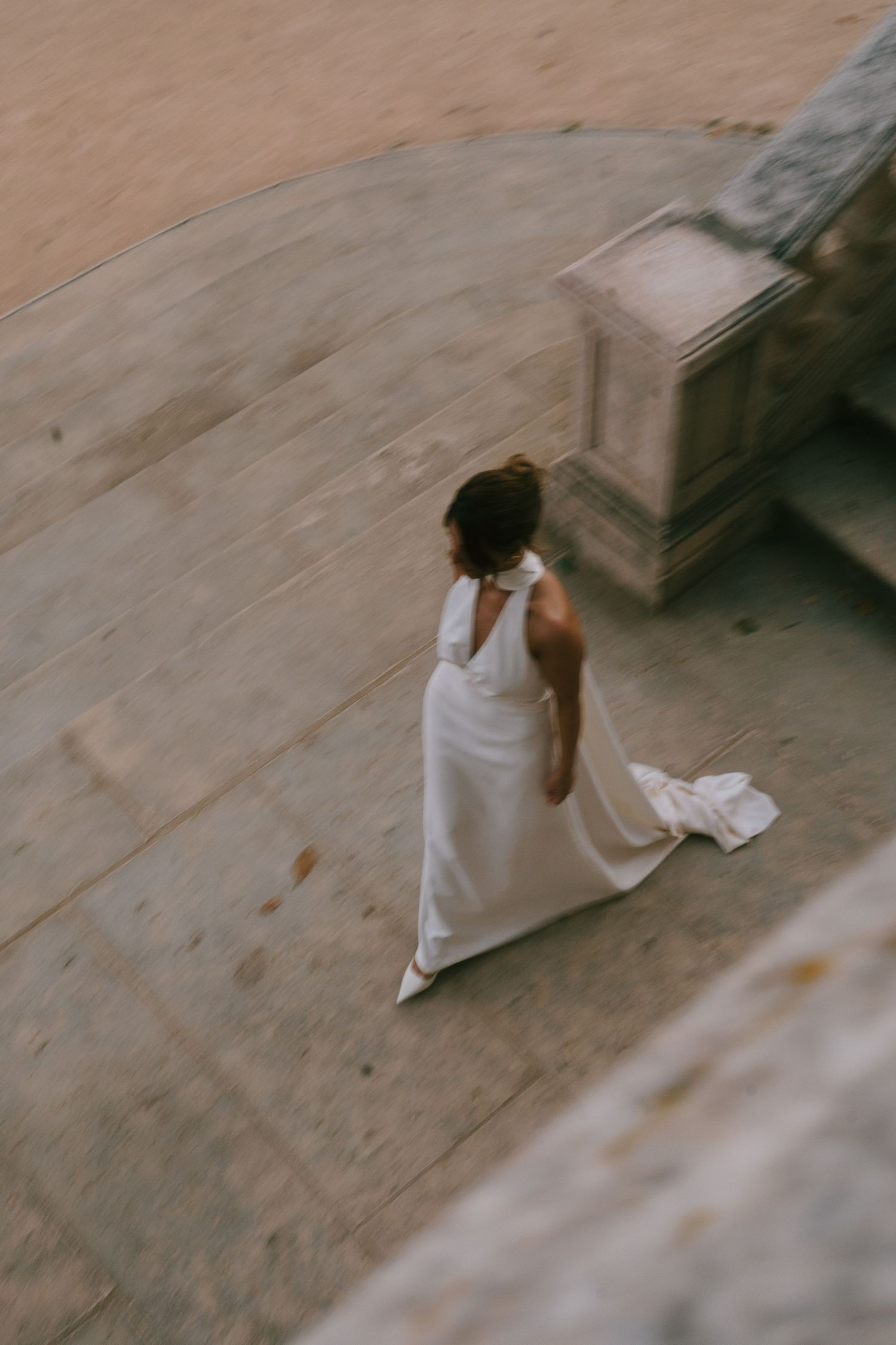 Figure in flowing white dress walking across a light stone surface.
