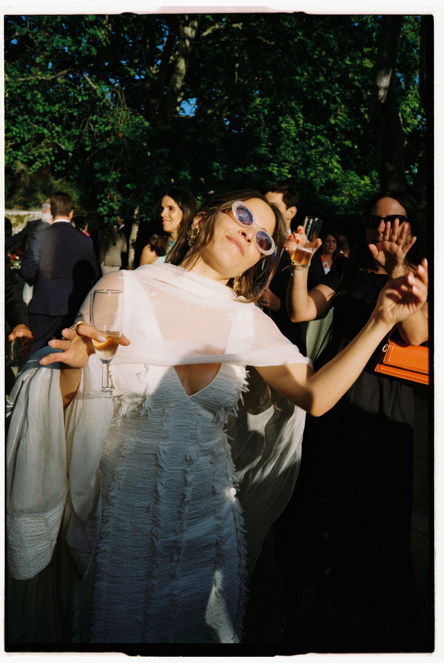 Wedding celebration with dancers in white dresses moving in sunlit outdoor setting.
