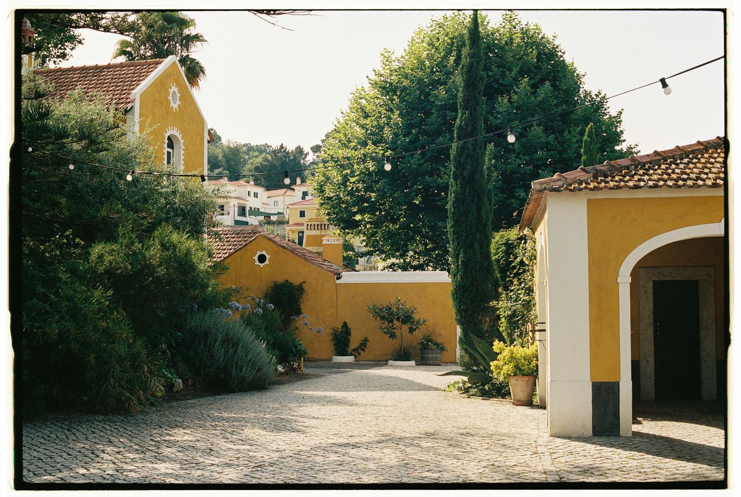 Series of yellow Mediterranean buildings connected by stone pathways under bright sunlight.