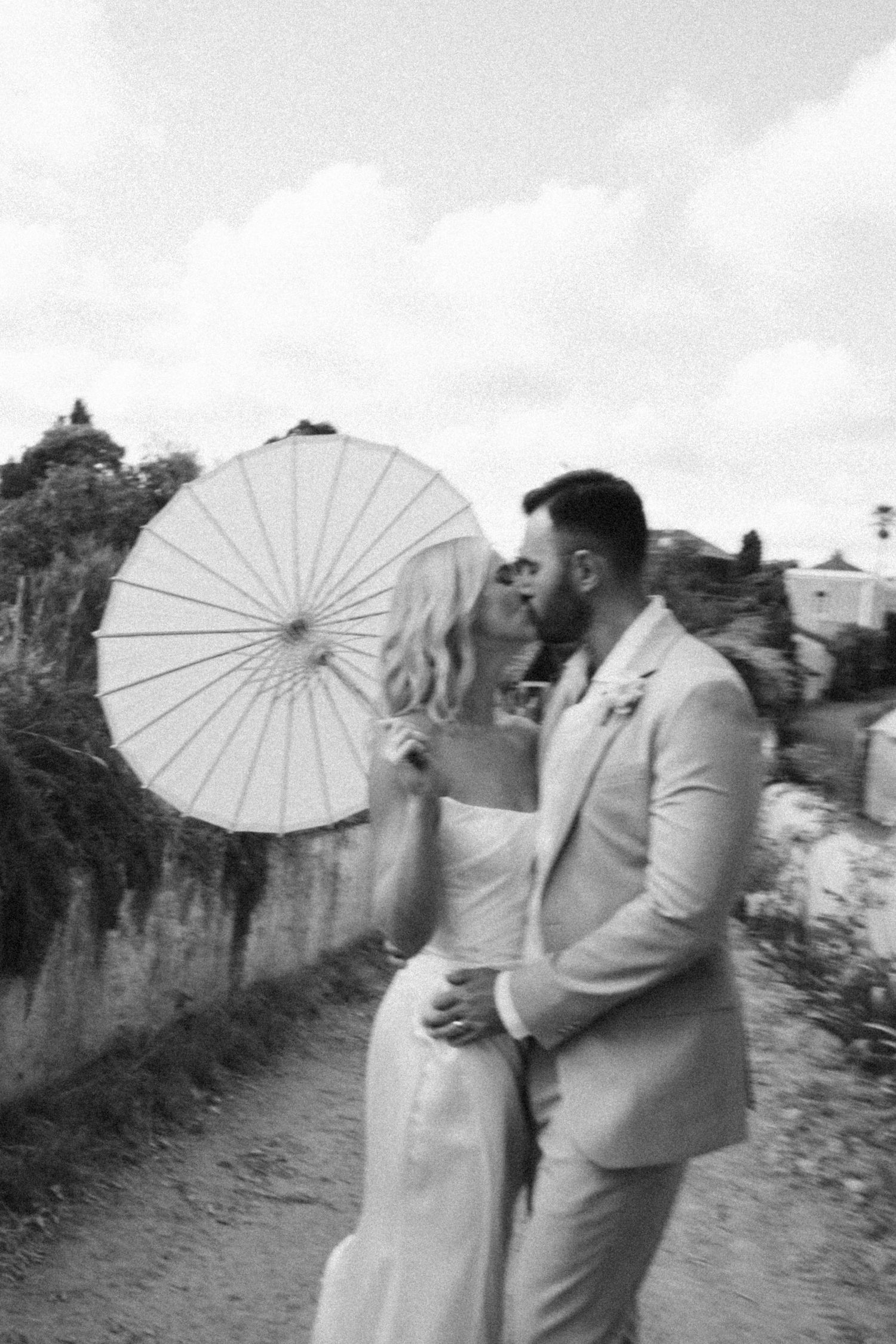 A couple sharing an intimate moment under a white parasol on a sunny path.