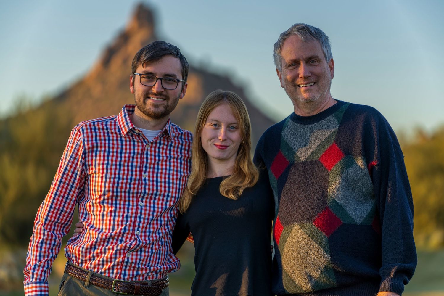 Group portrait of people wearing casual attire standing together outdoors at dusk.