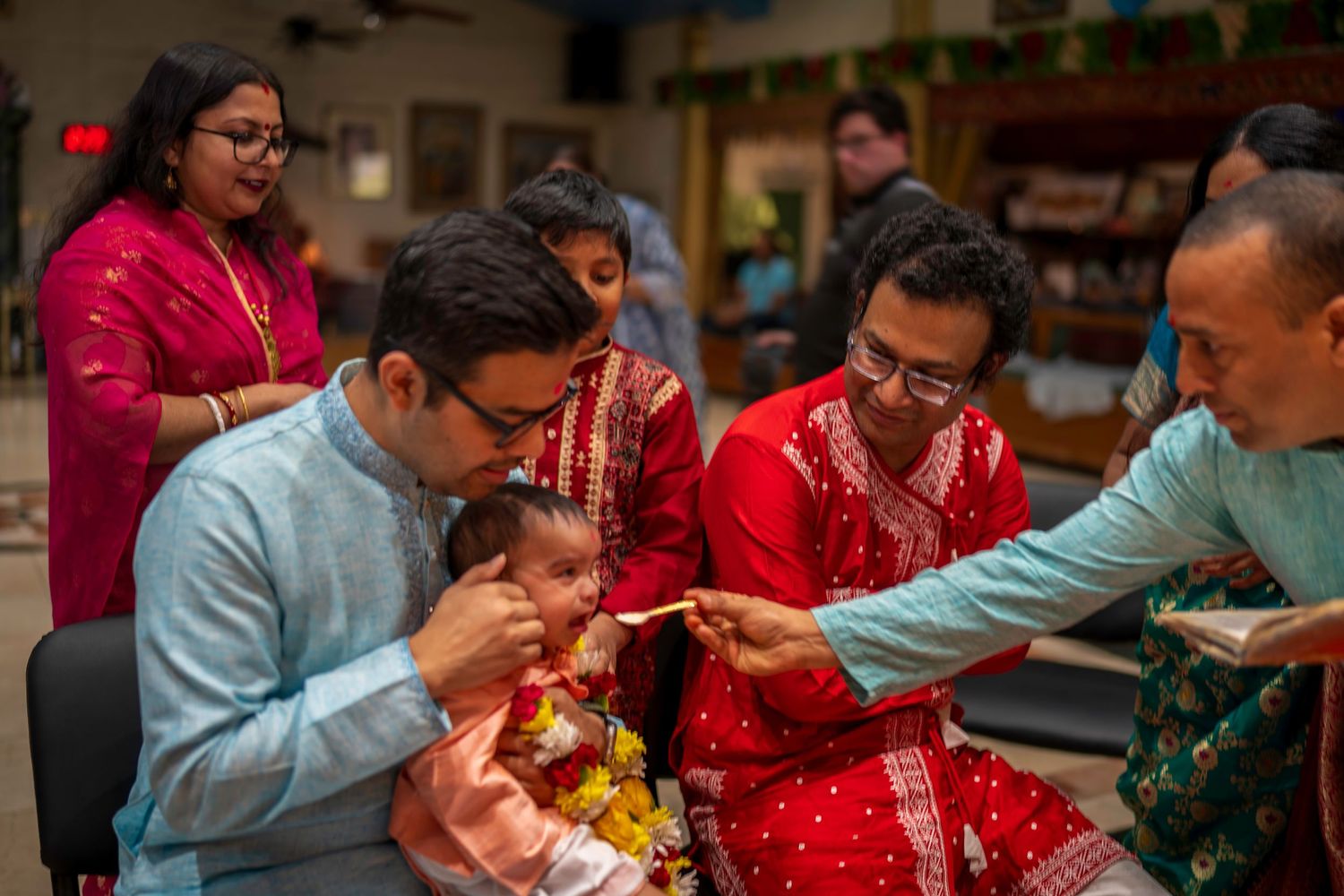Family gathered for a traditional South Asian annaprashana rice feeding ceremony with baby in festive red attire.