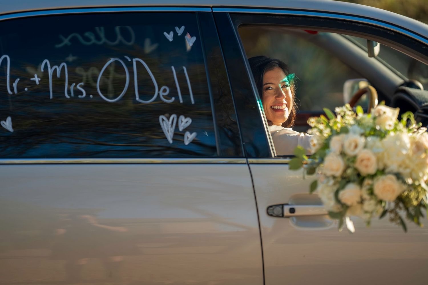 Smiling bride looks out car window decorated with Mr. and Mrs. ODell for wedding getaway.