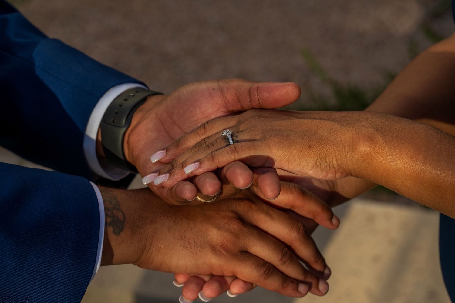 Close-up of couple's hands stacked together showing engagement ring and wedding bands during romantic ceremony.