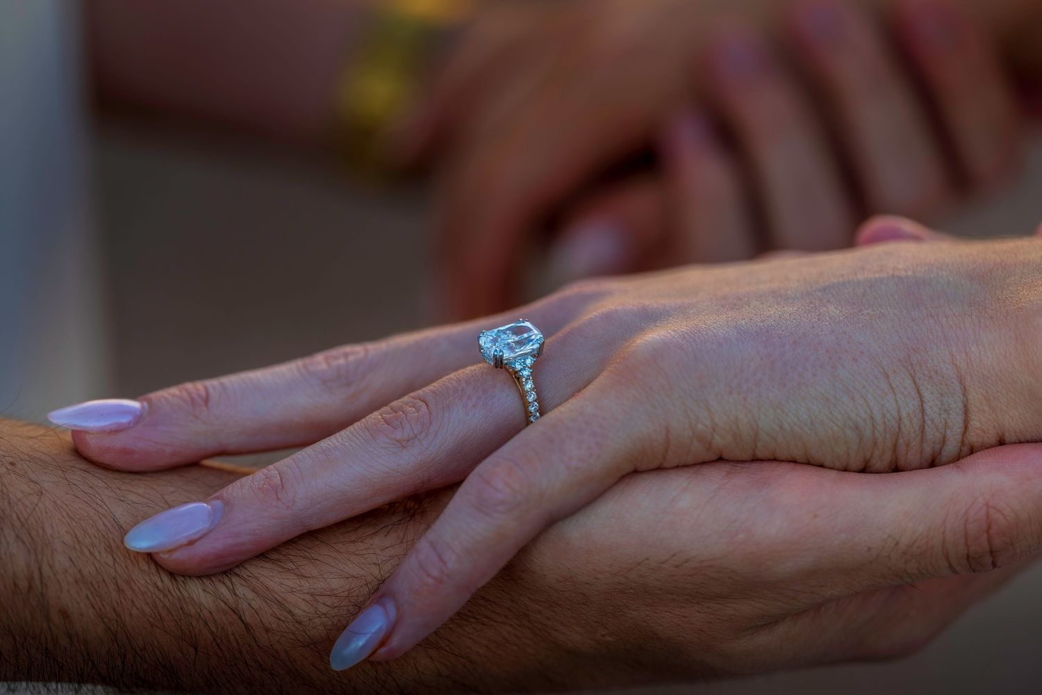Detail shot of hands with engagement ring during golden hour photography session.