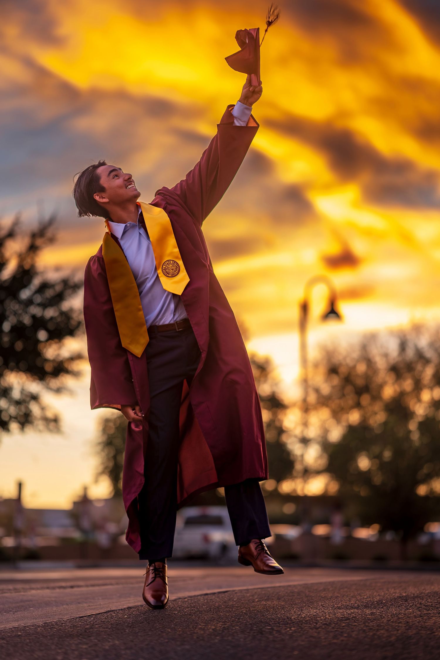 Dramatic sunset graduation photos with student in maroon gown striking dynamic poses.