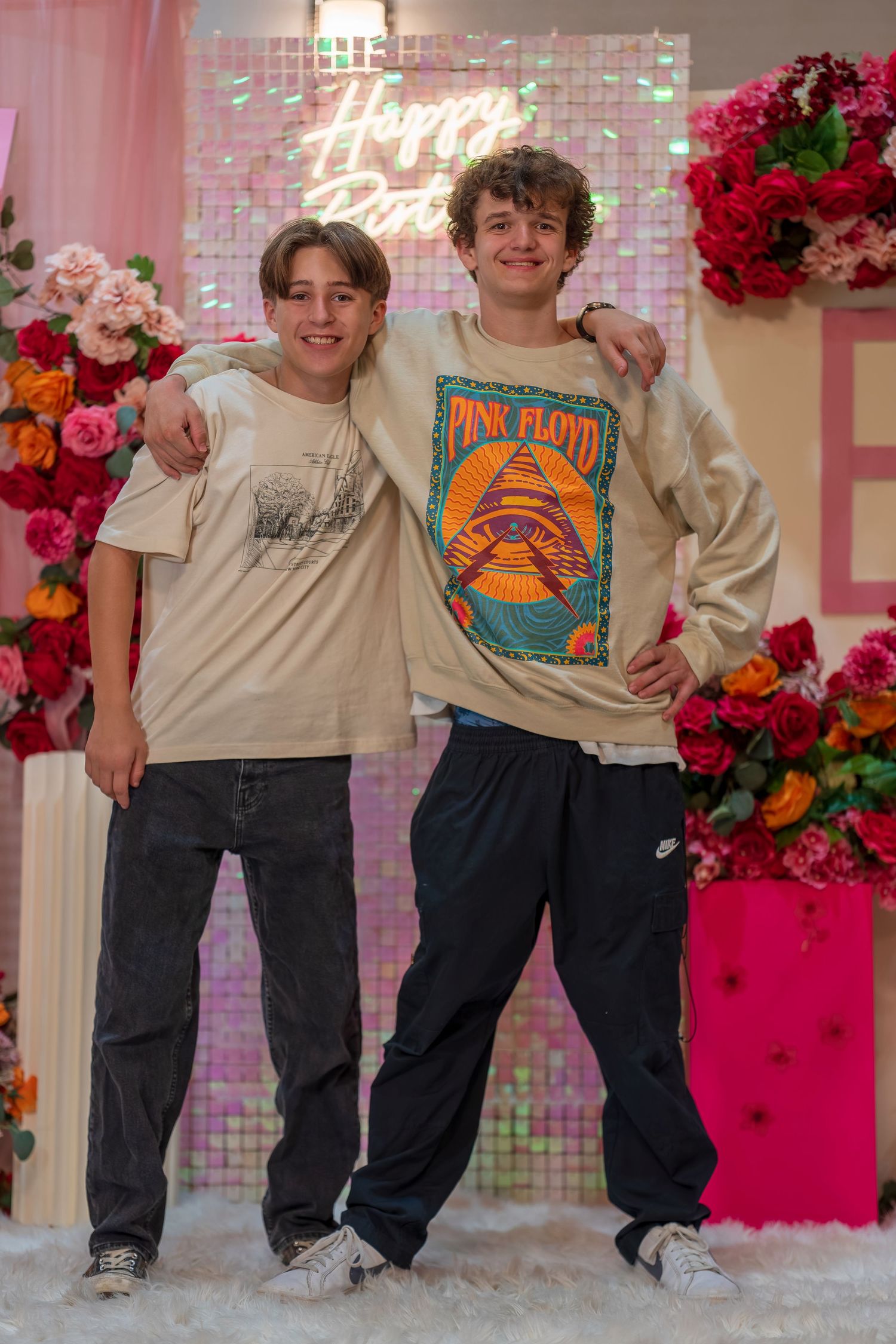 Friends in matching beige tops and jeans posing together against a pink floral backdrop.
