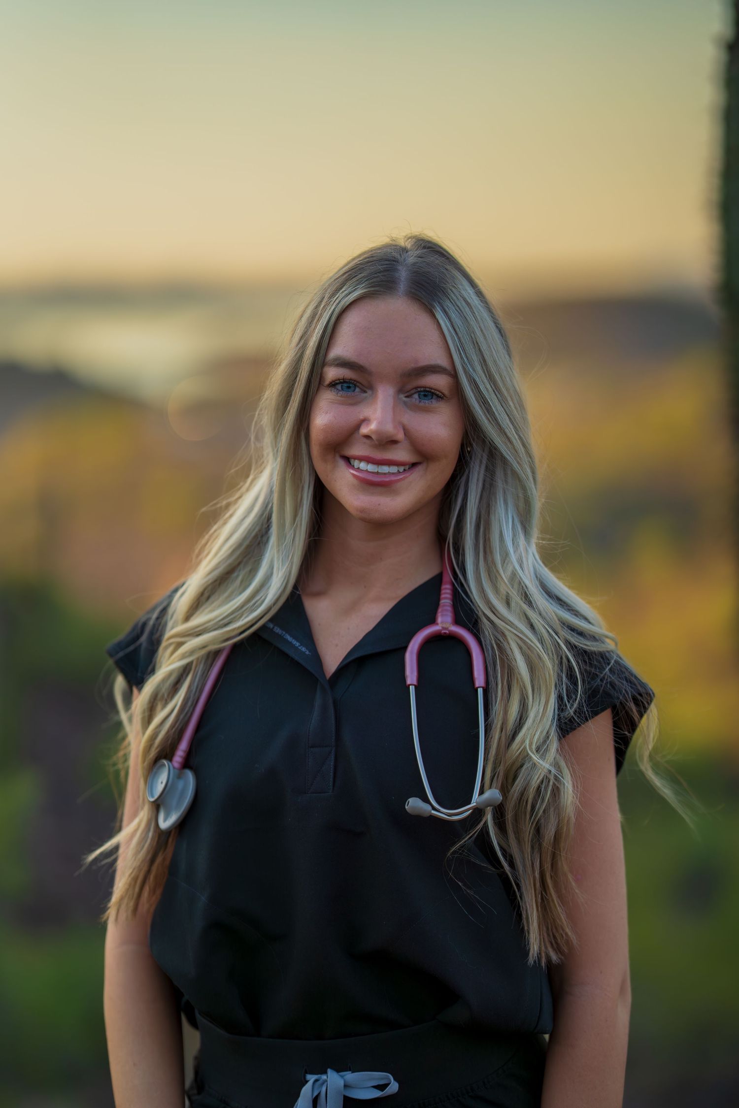 Healthcare worker in black uniform smiles warmly during outdoor desert photoshoot.