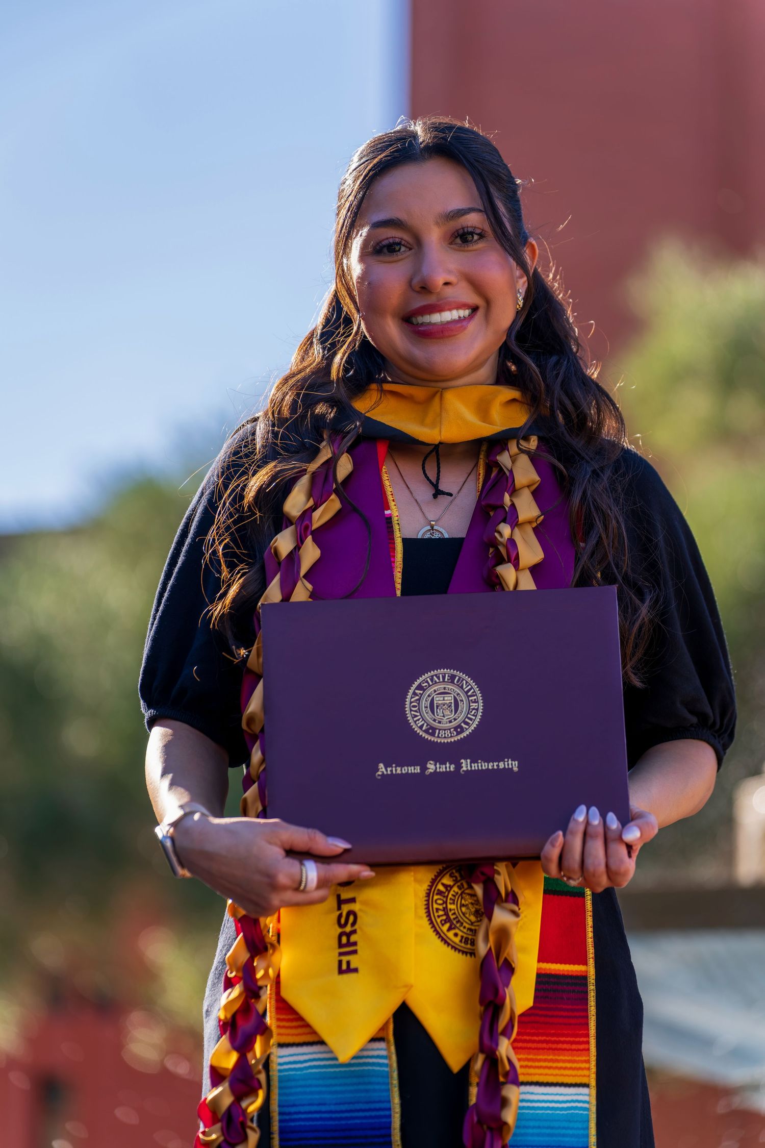 Graduate displays purple diploma holder while wearing colorful graduation stole.