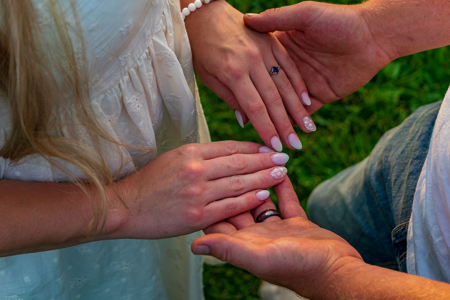 Hands exchanging rings during outdoor wedding ceremony.