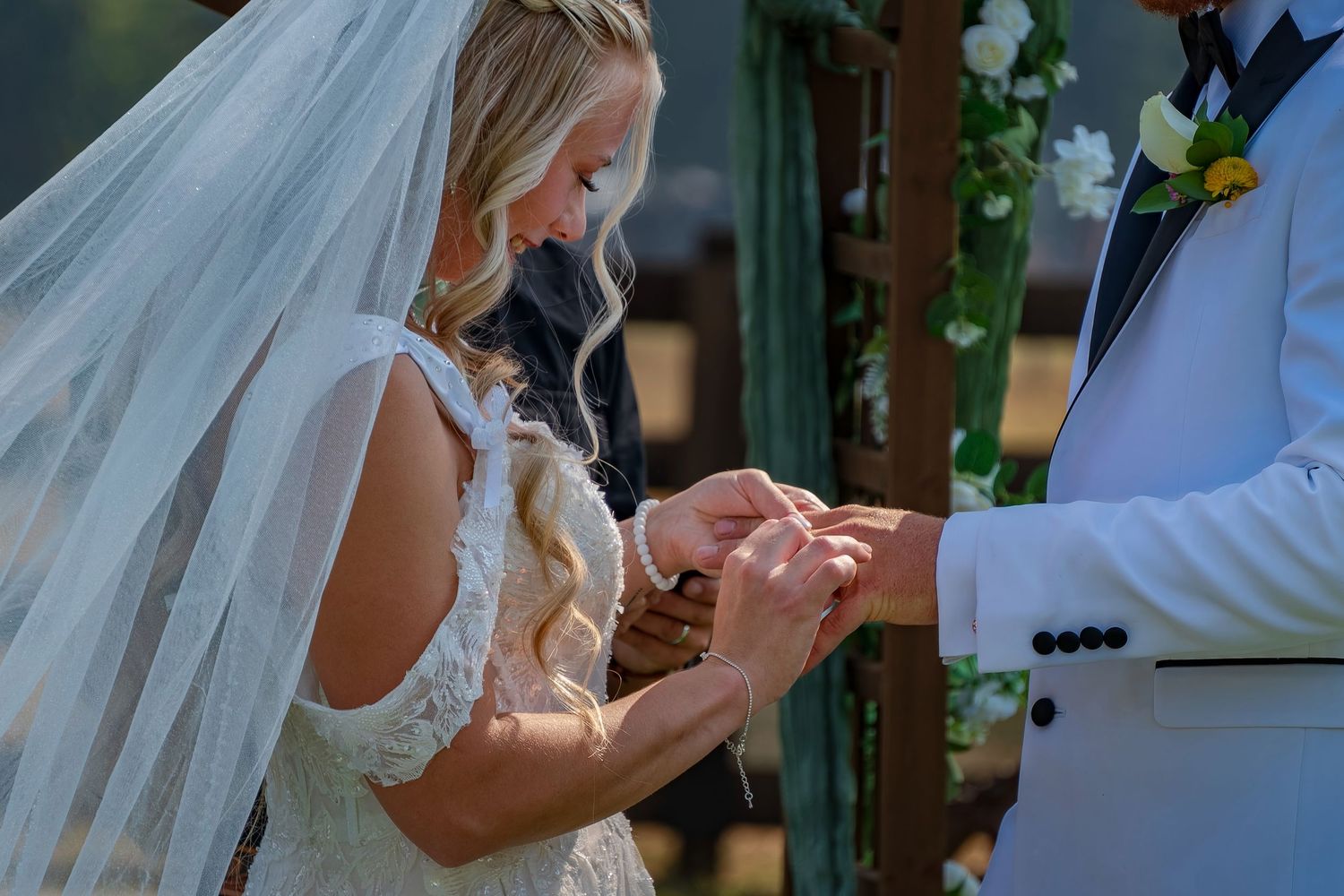 Close-up of ring exchange during rustic outdoor wedding ceremony with greenery backdrop.
