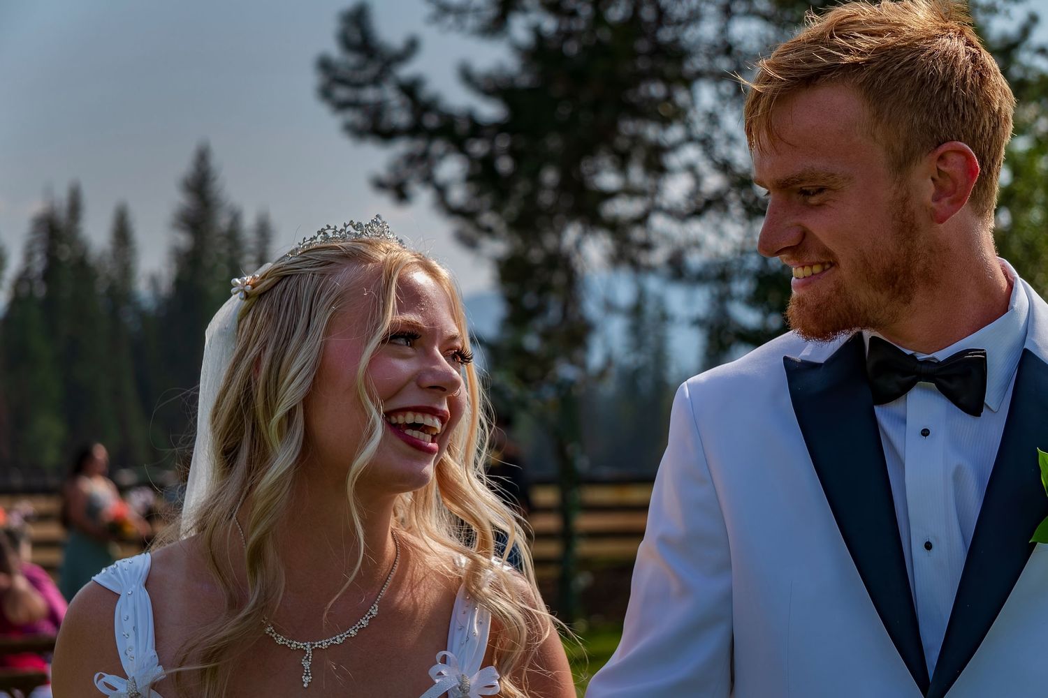 Wedding couple shares authentic laughter against a backdrop of pine trees.