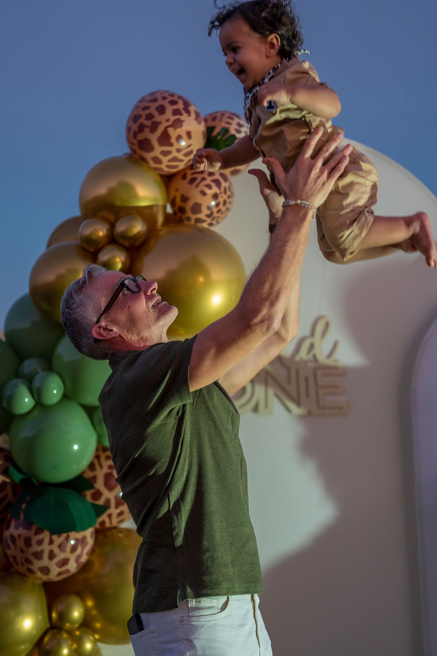 A joyful moment captured at a safari-themed celebration with gold balloons and decorative giraffes.