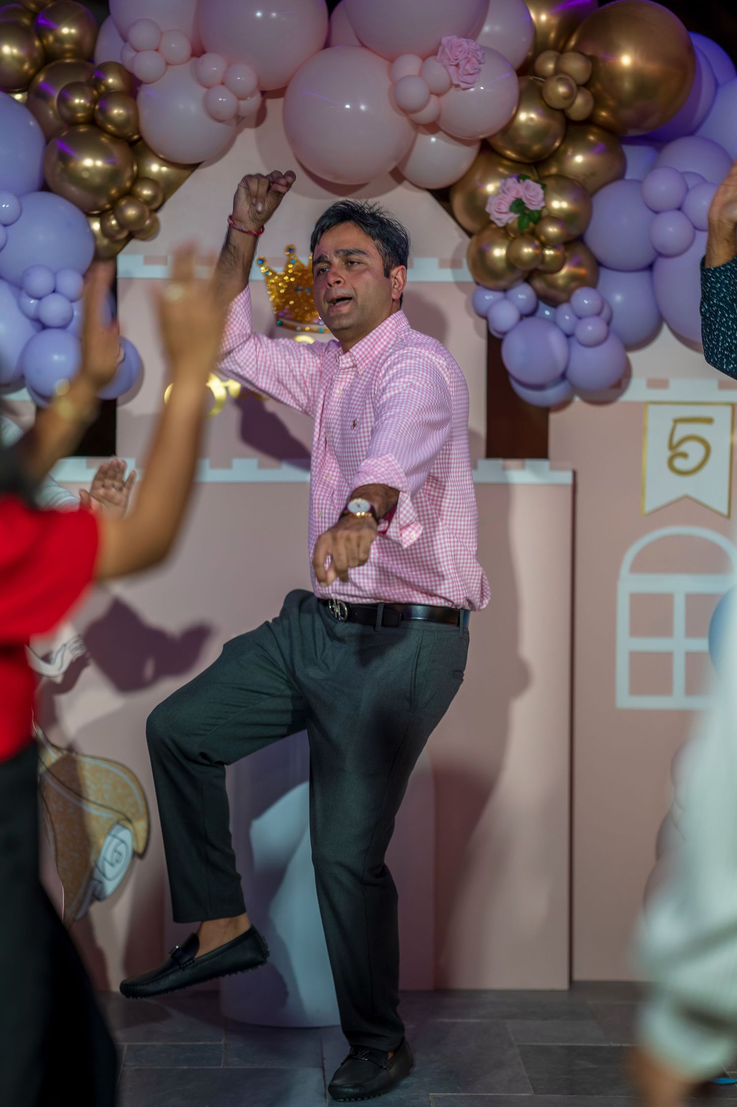 Person in pink shirt and dark pants dancing under balloon decorations at a party.