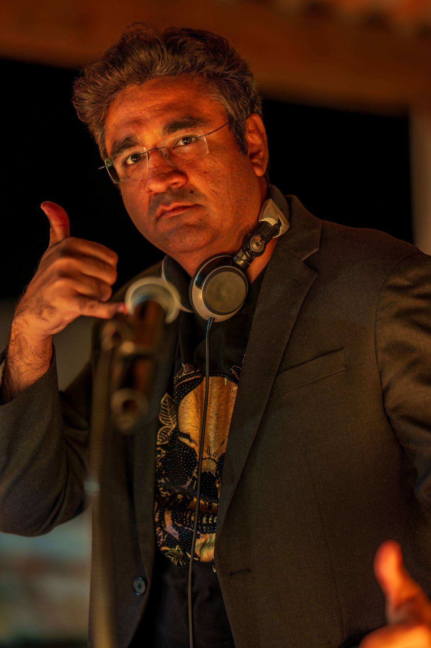 A person in a dark suit jacket speaks into a microphone in warm lighting.
