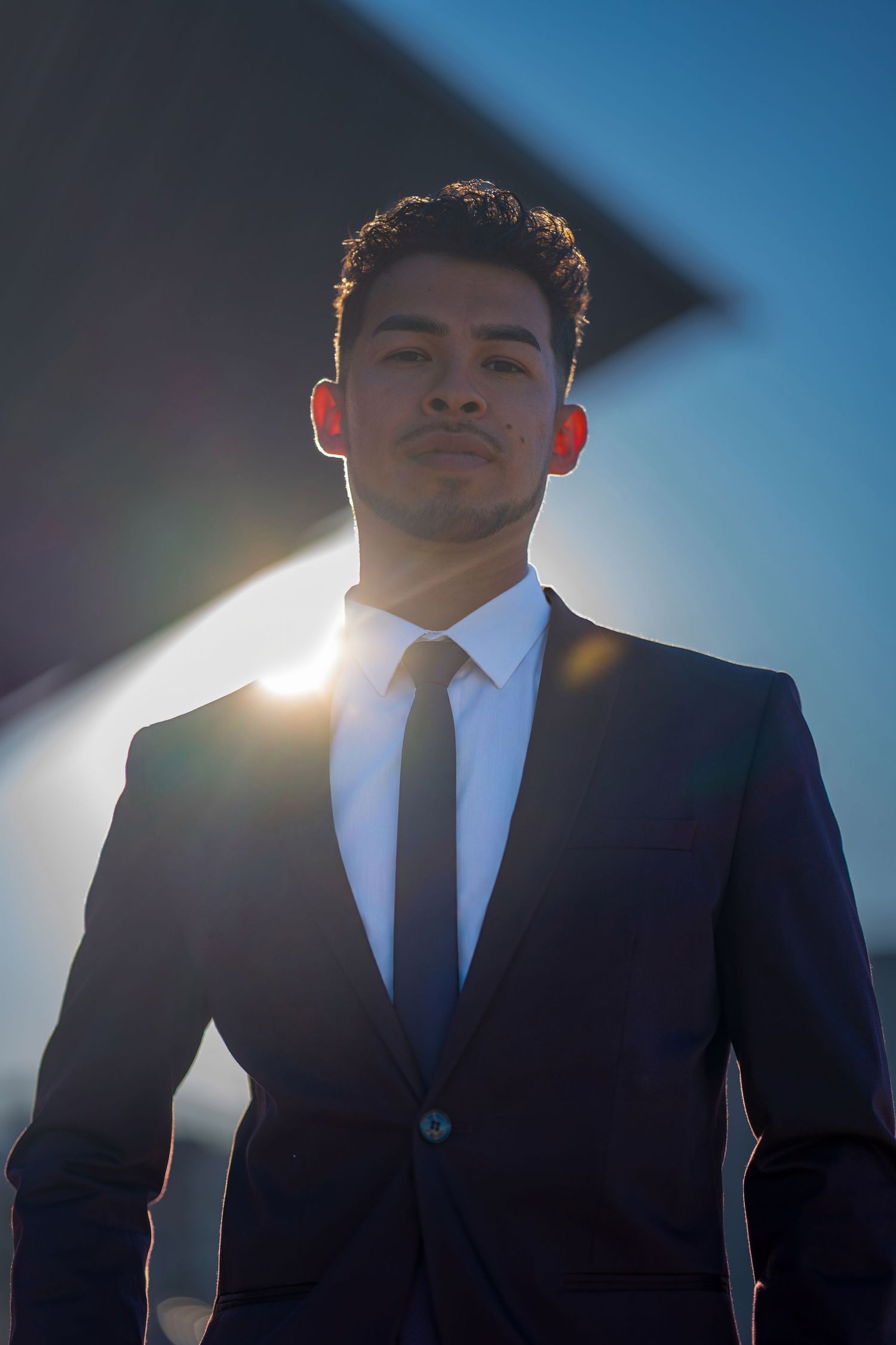 Low angle portrait of person in business attire with dramatic sunlight and architectural elements.