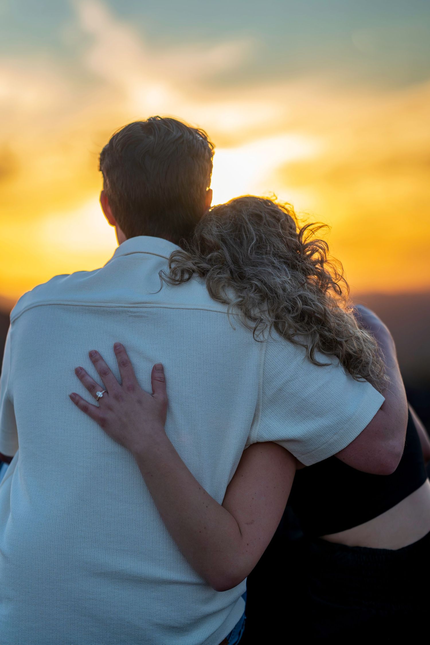 A couple embraces and watches a stunning golden sunset together from behind.
