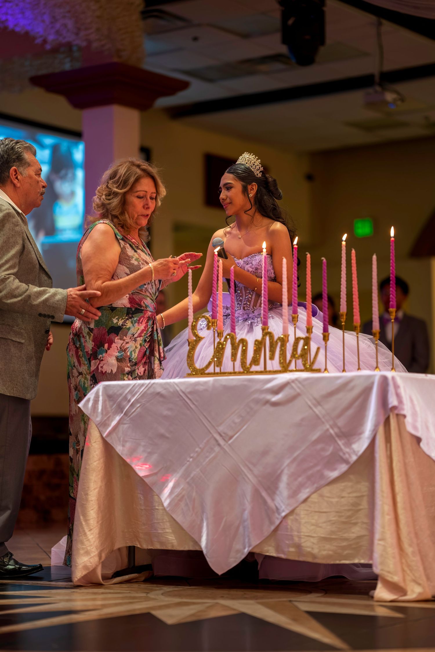 Emma's quinceañera candle lighting ceremony with family at decorated table with pink candles and gold name sign.