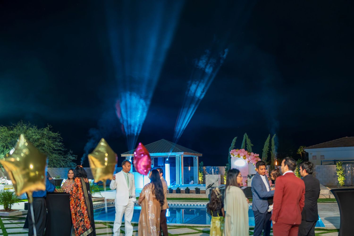 People gather for an outdoor nighttime celebration with blue spotlights illuminating the scene.