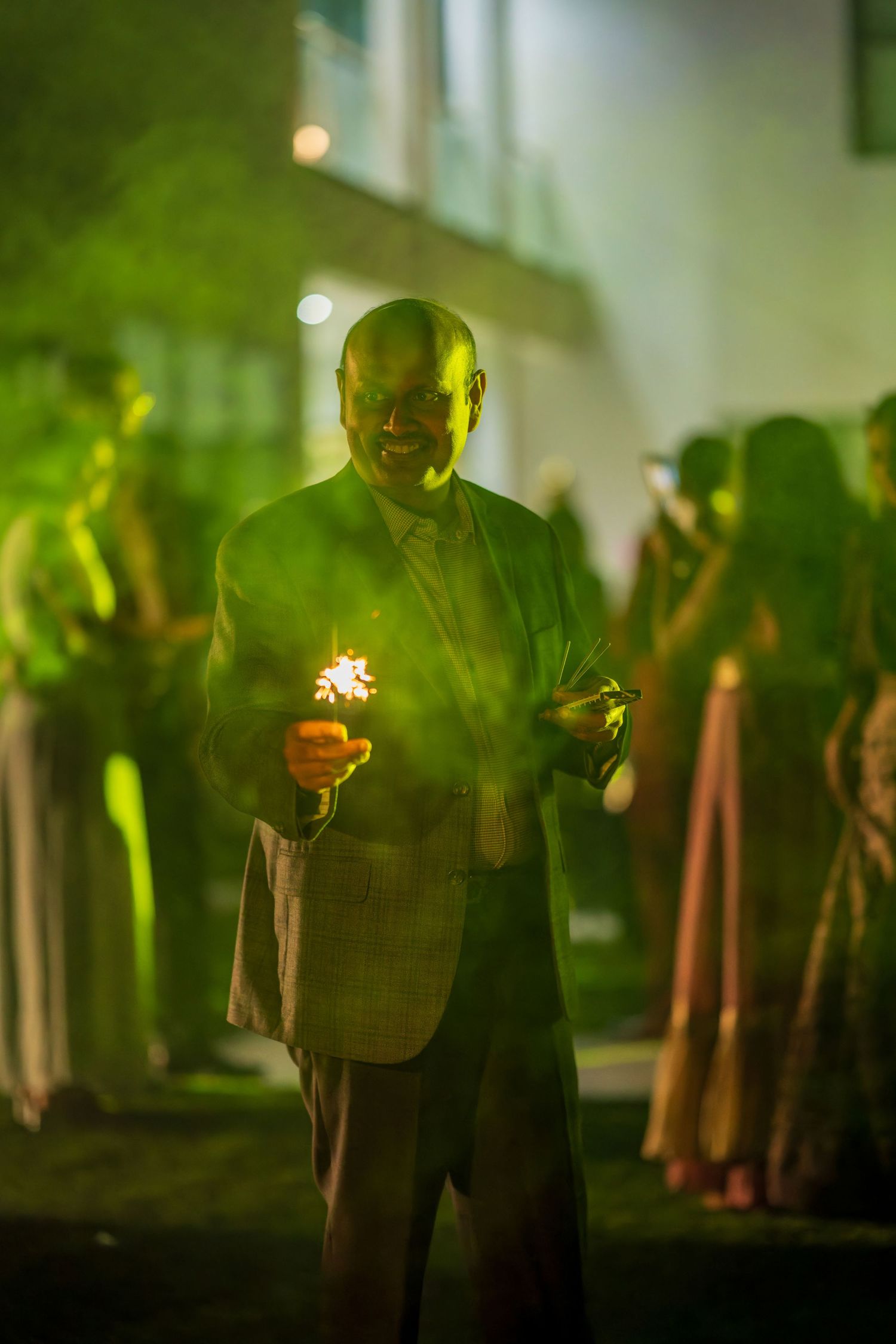Person holding sparklers in green-tinted lighting during nighttime celebration.