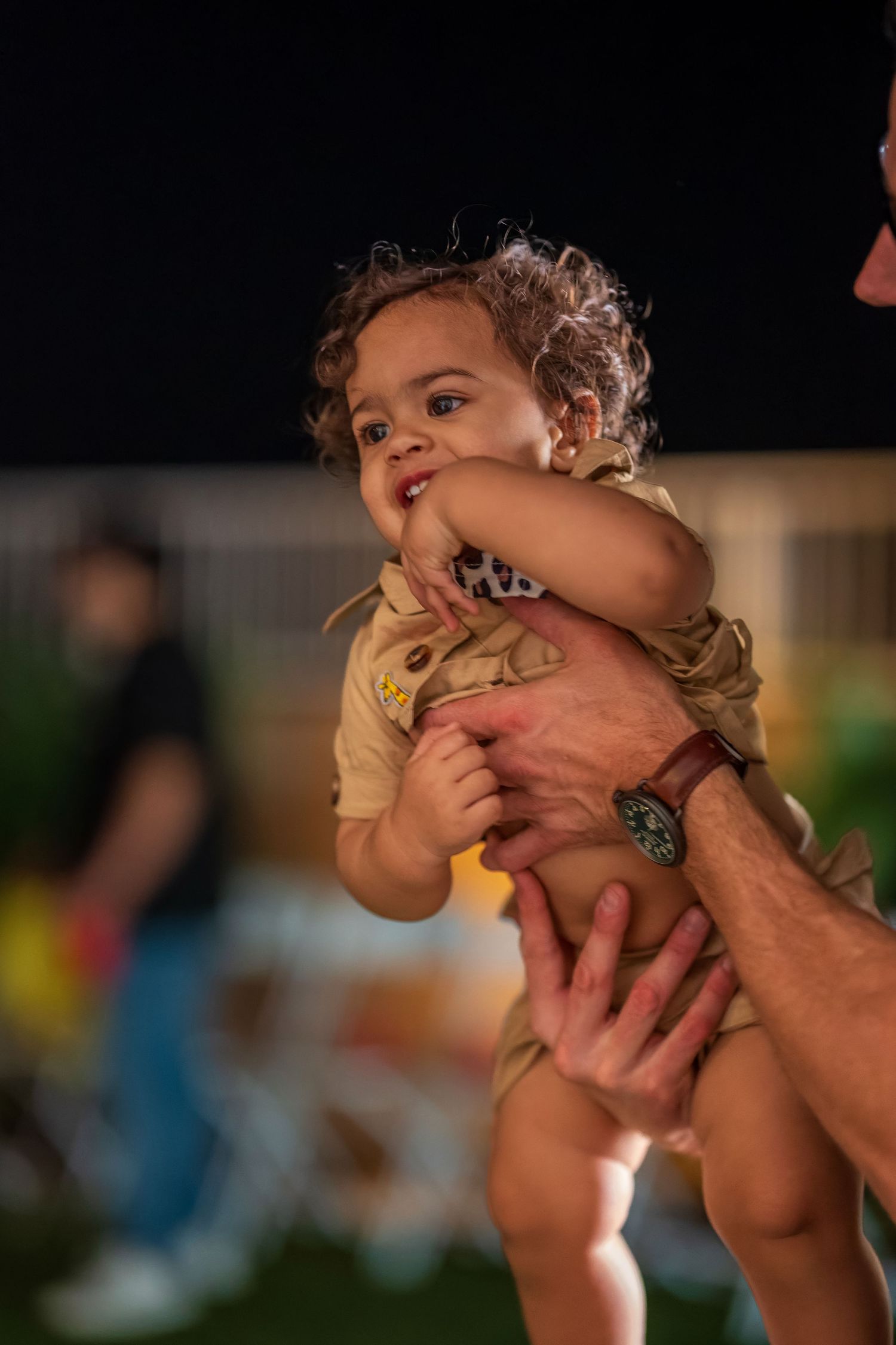 A small child in a yellow outfit being held up and giggling during a playful moment.