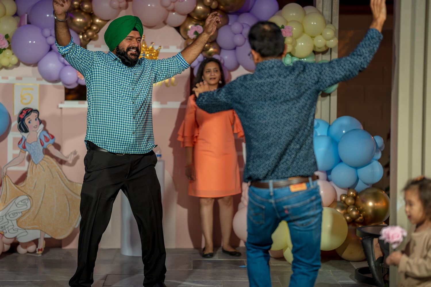Guests dancing and celebrating at a festive party with purple and gold balloons decorating the venue.