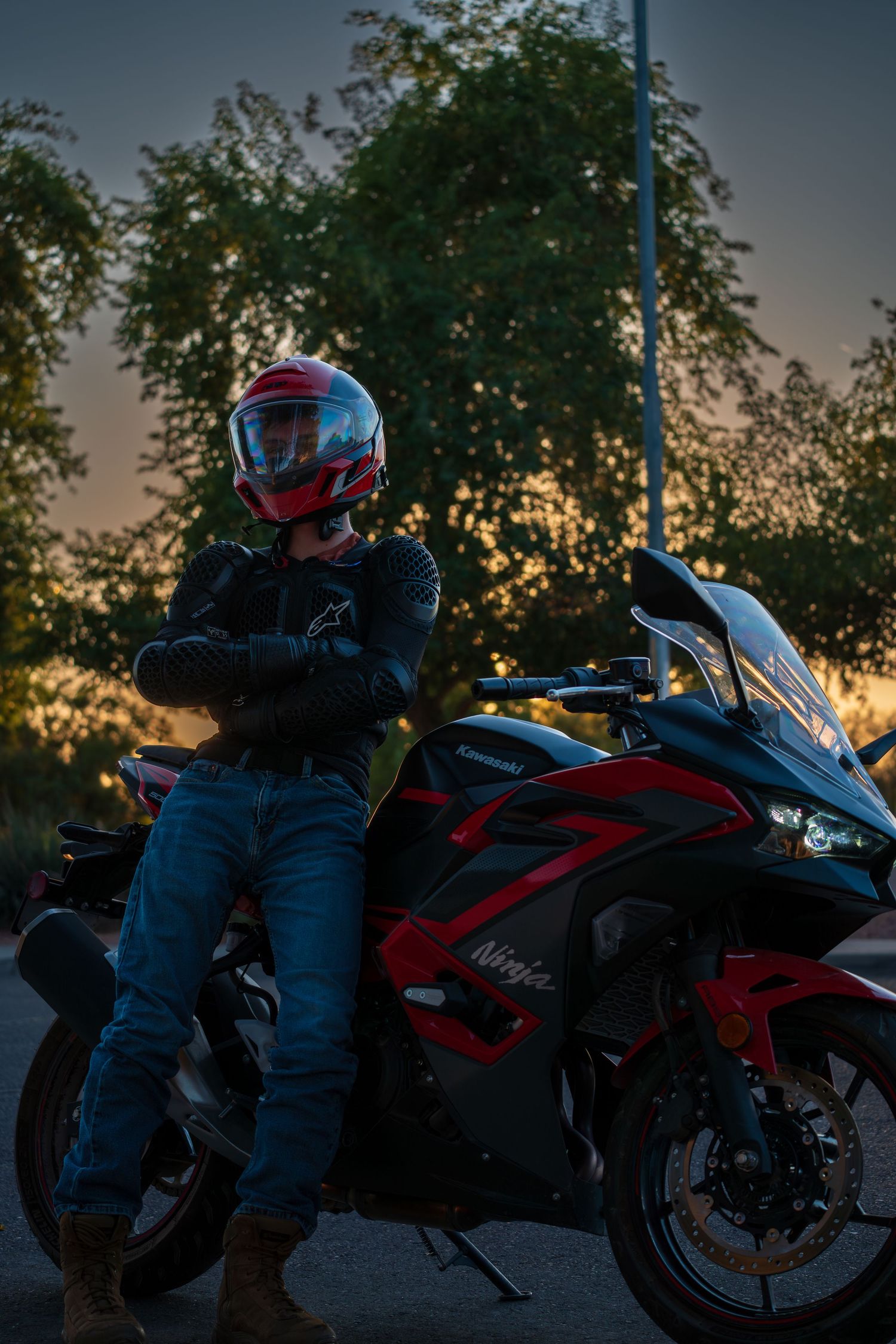Motorcyclist in protective gear sitting on red sport bike at dusk.