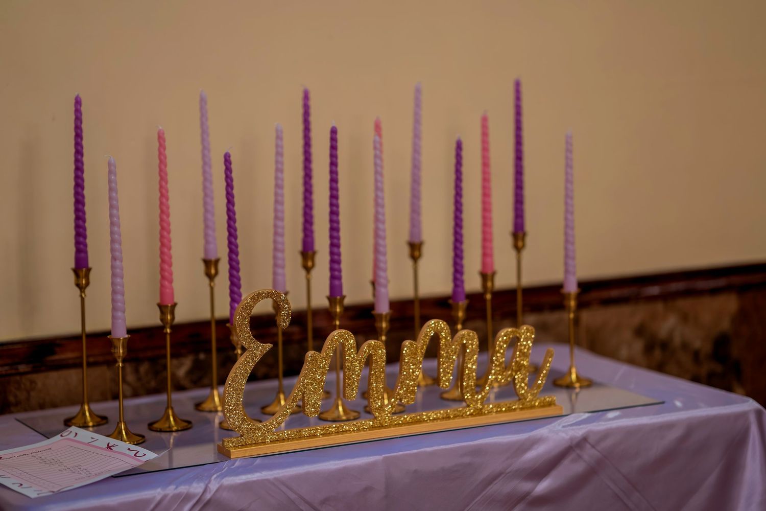 Gold letter name sign Emma displayed among purple and pink twisted taper candles on a lavender tablecloth.
