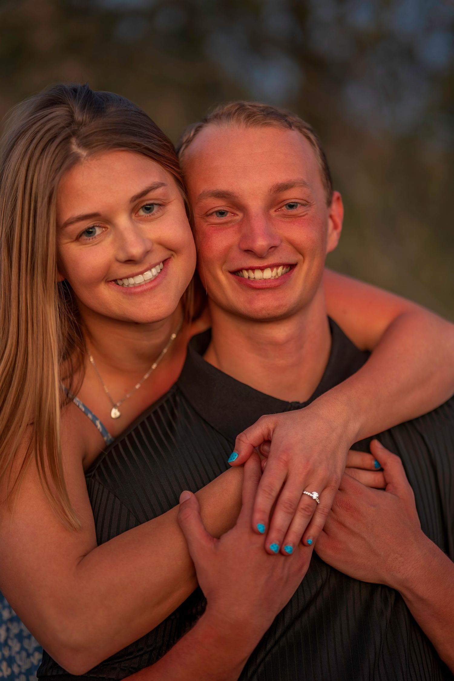 A happy couple embraces and smiles warmly in golden sunset light.