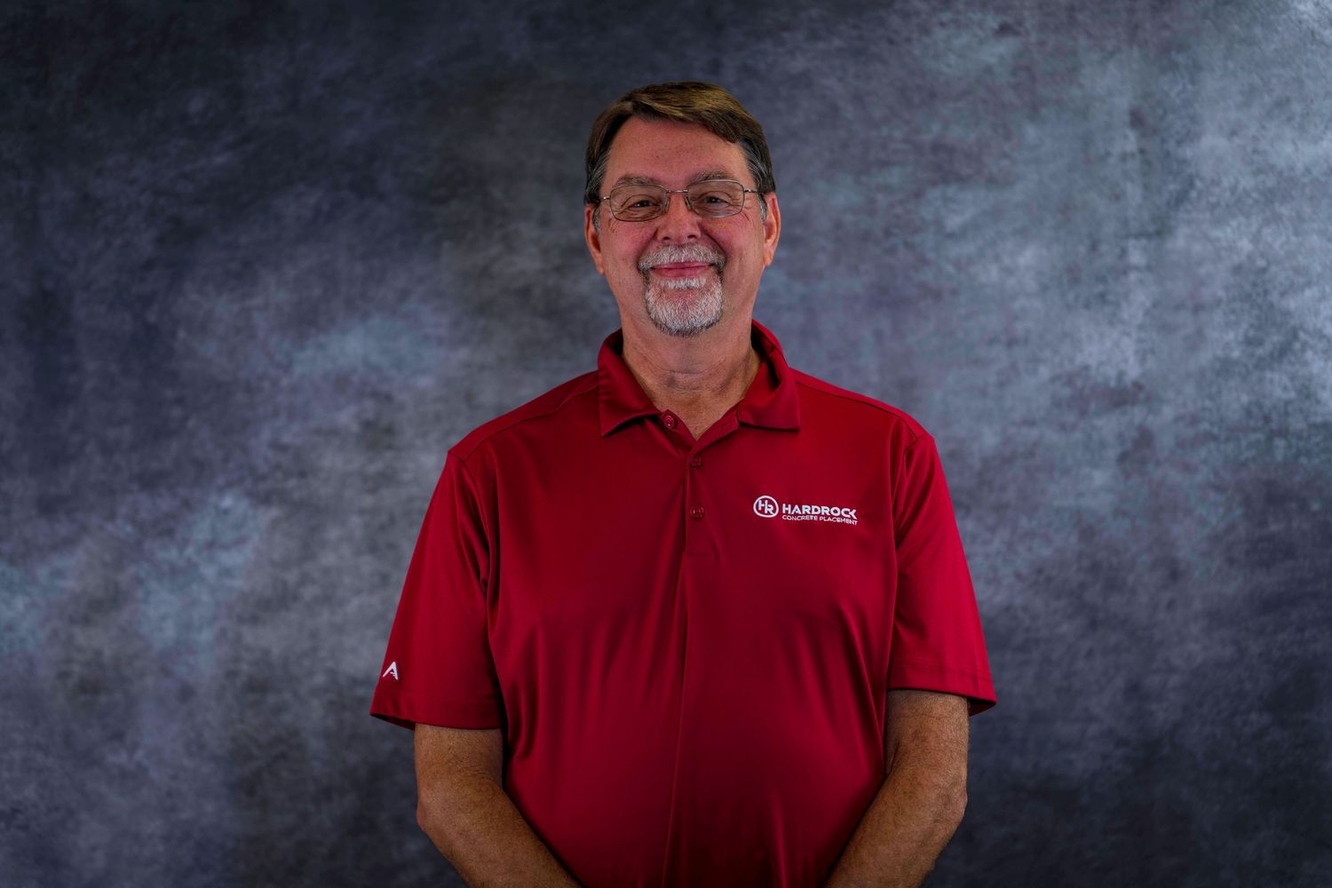 Cheerful person in red company polo shirt photographed against textured gray background.