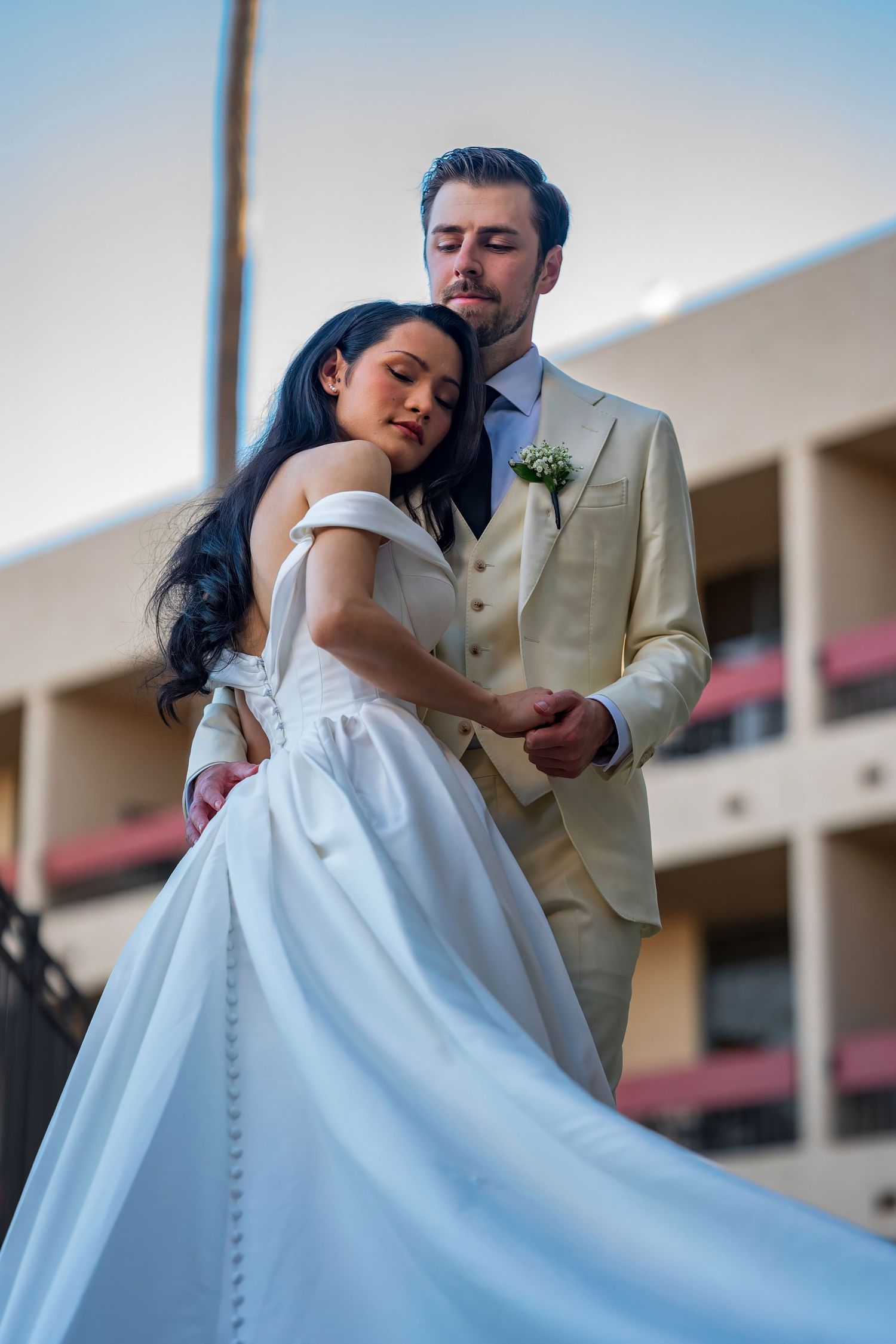 A romantic wedding portrait showing a couple embracing, with the bride in a flowing white gown against an urban backdrop.