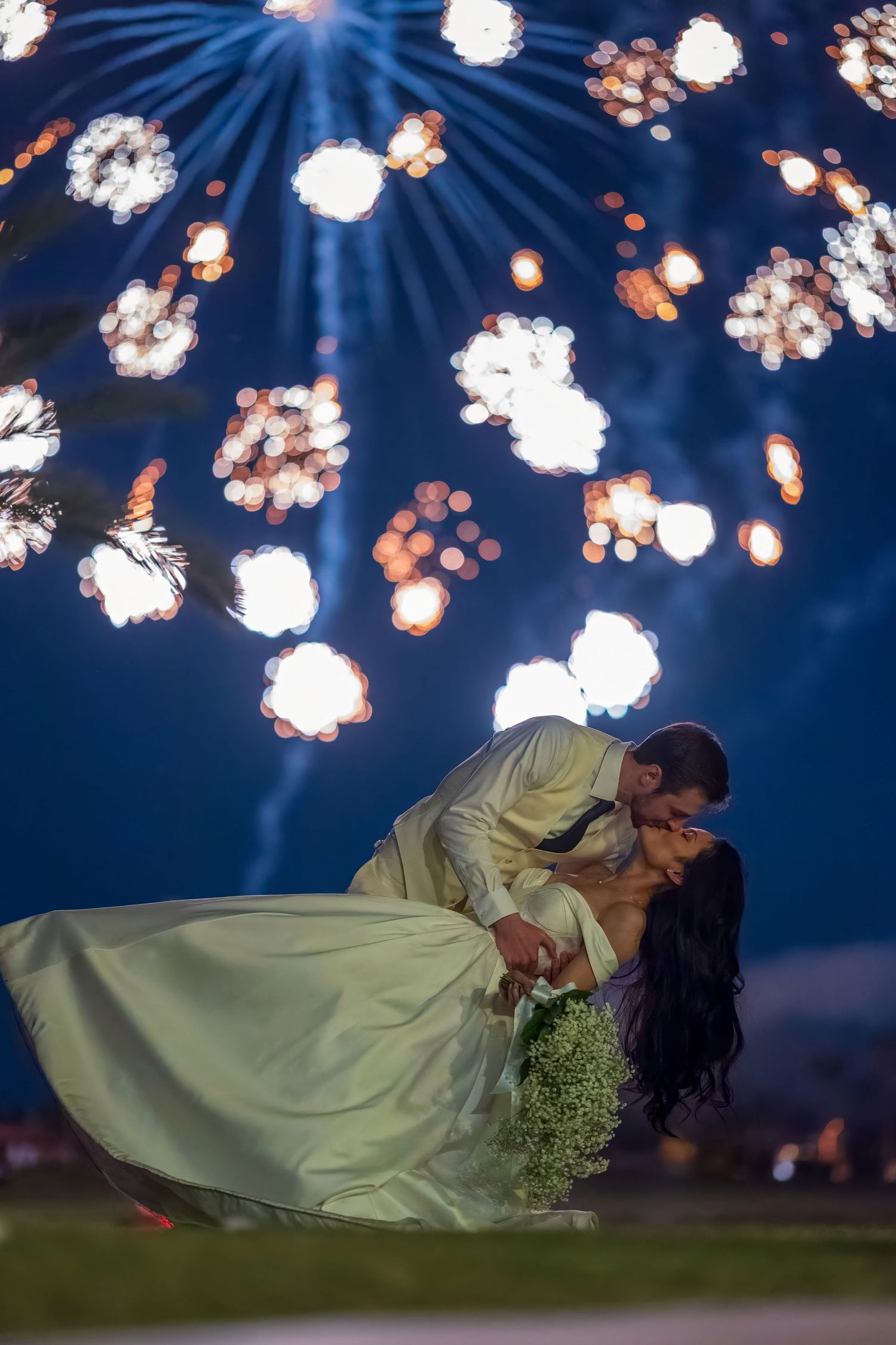 Romantic wedding couple embraces under blue fireworks display in dramatic nighttime photo shoot.