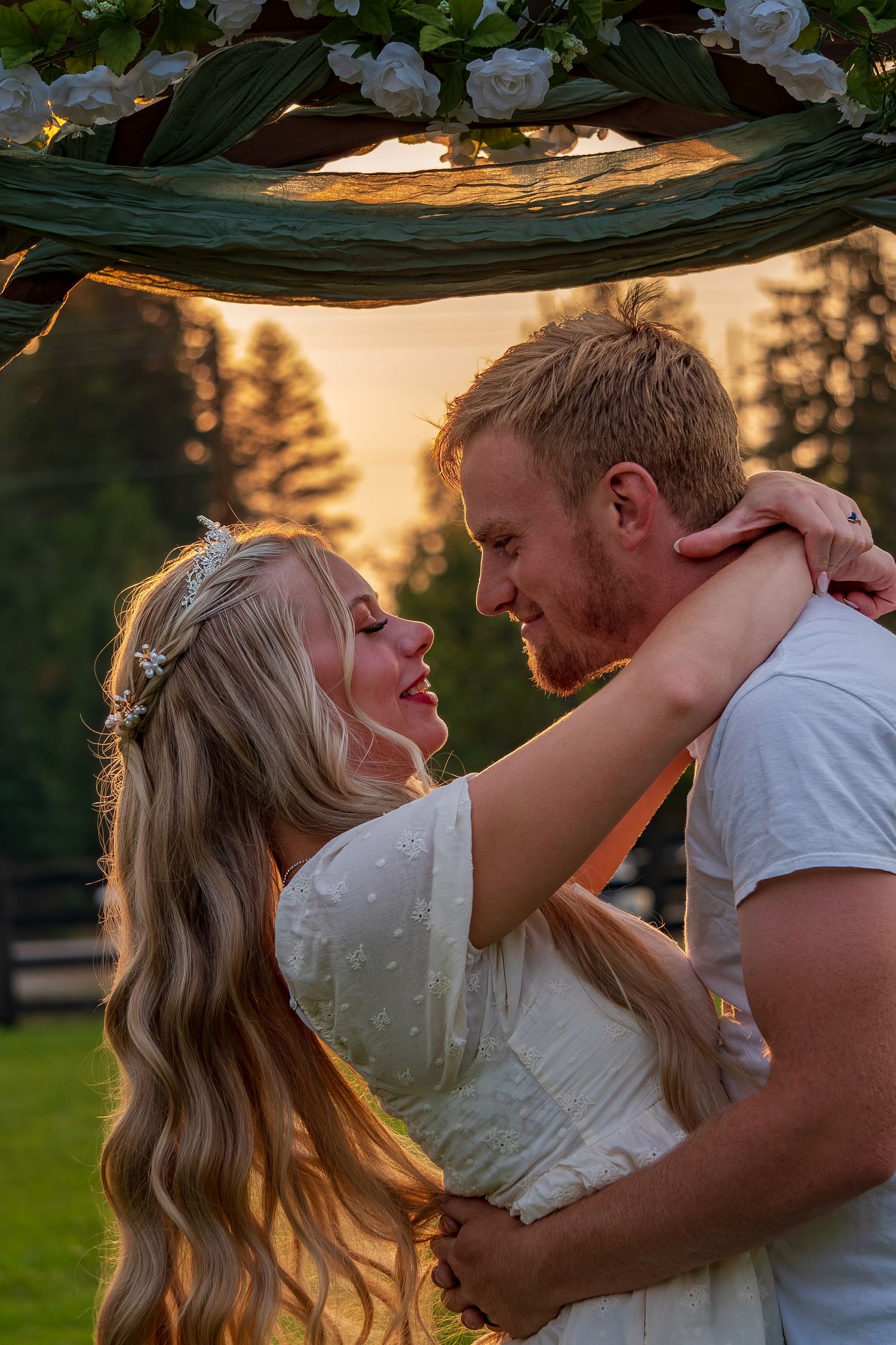 Intimate moment shared under floral arch at golden hour.