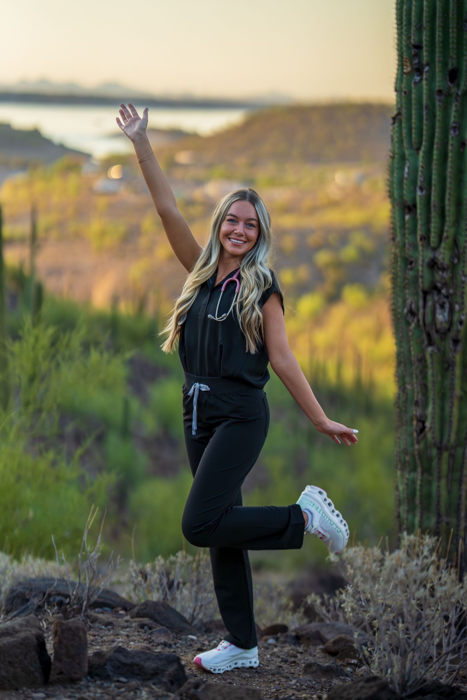 Playful healthcare worker leaps joyfully among desert cacti during sunset photo session.