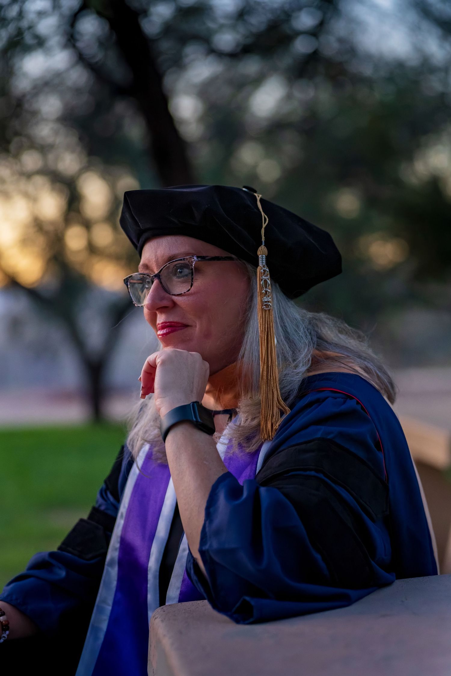 Contemplative graduation portrait showing graduate in traditional academic dress at dusk.