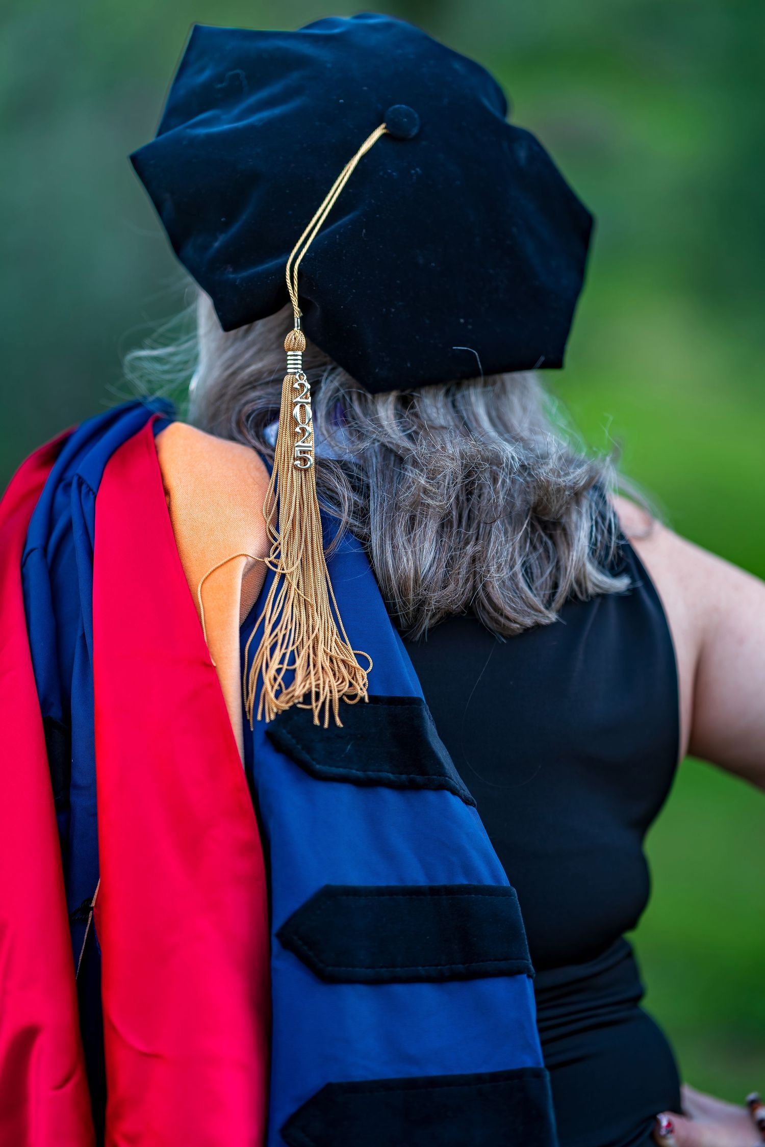 Close-up of gold graduation tassel against blue doctoral hood and regalia.