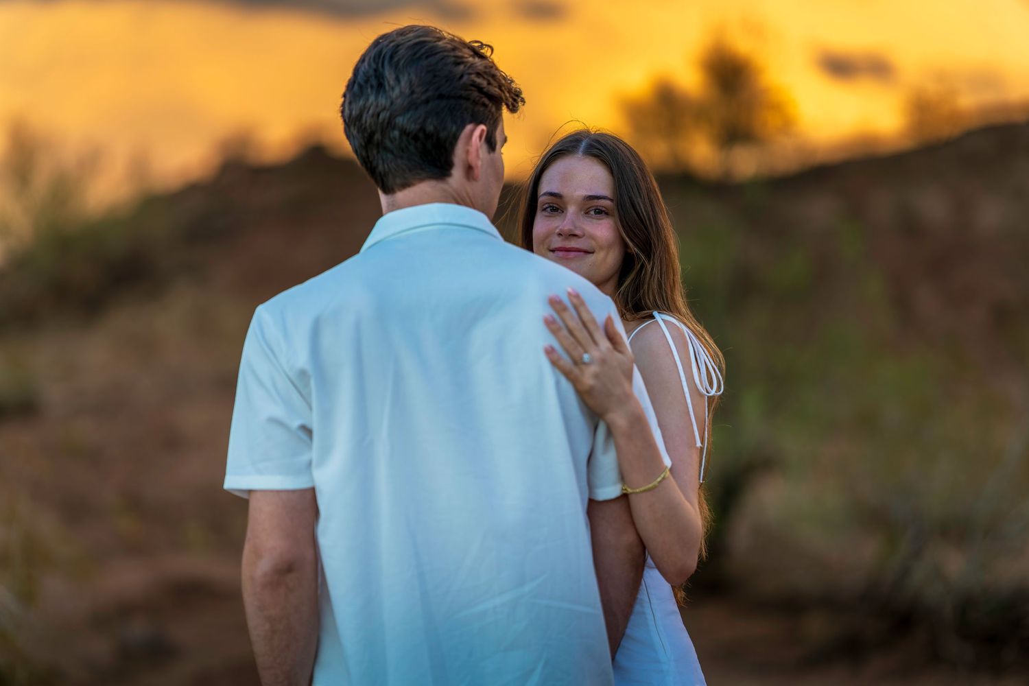 Couple in white clothing sharing tender moment at sunset in desert landscape.