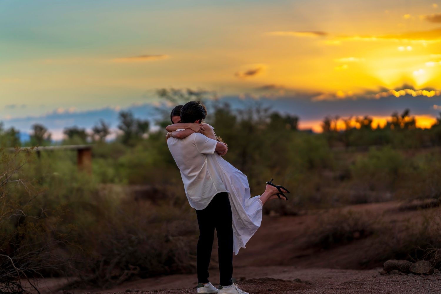 A couple embraces during their desert engagement session at sunset.
