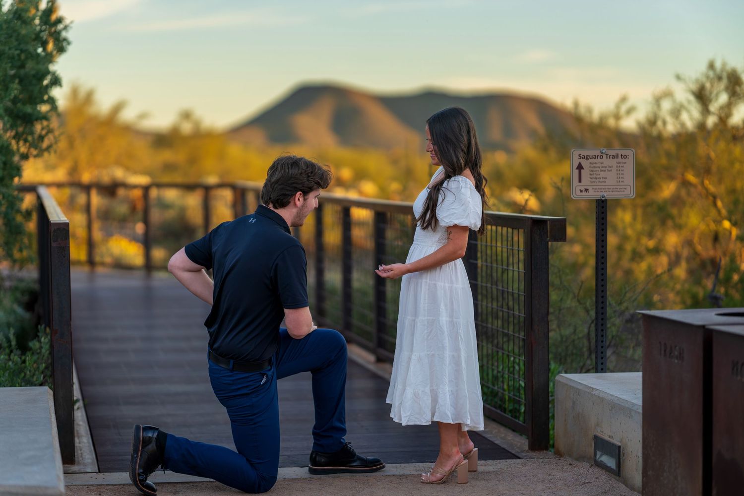 A proposal moment captured on a scenic bridge with desert mountains in the background at sunset.