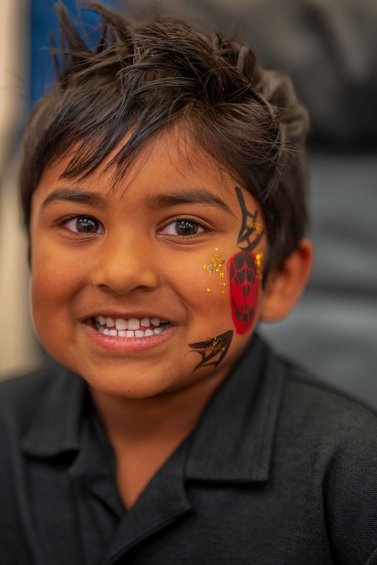 A smiling boy with Spider-Man face paint on his cheek poses for a portrait.