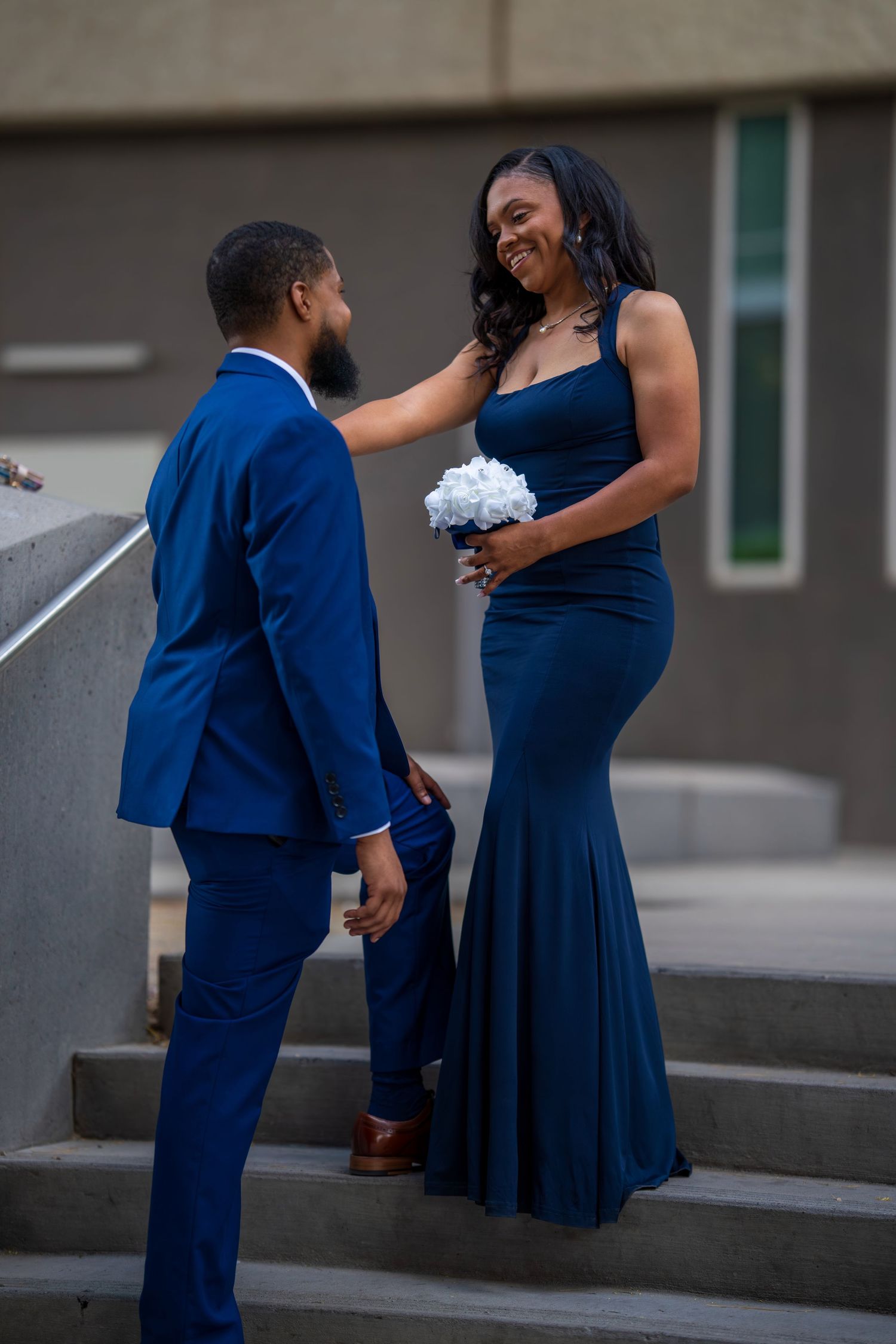 Man in blue suit and woman in navy gown share joyful moment on outdoor steps.