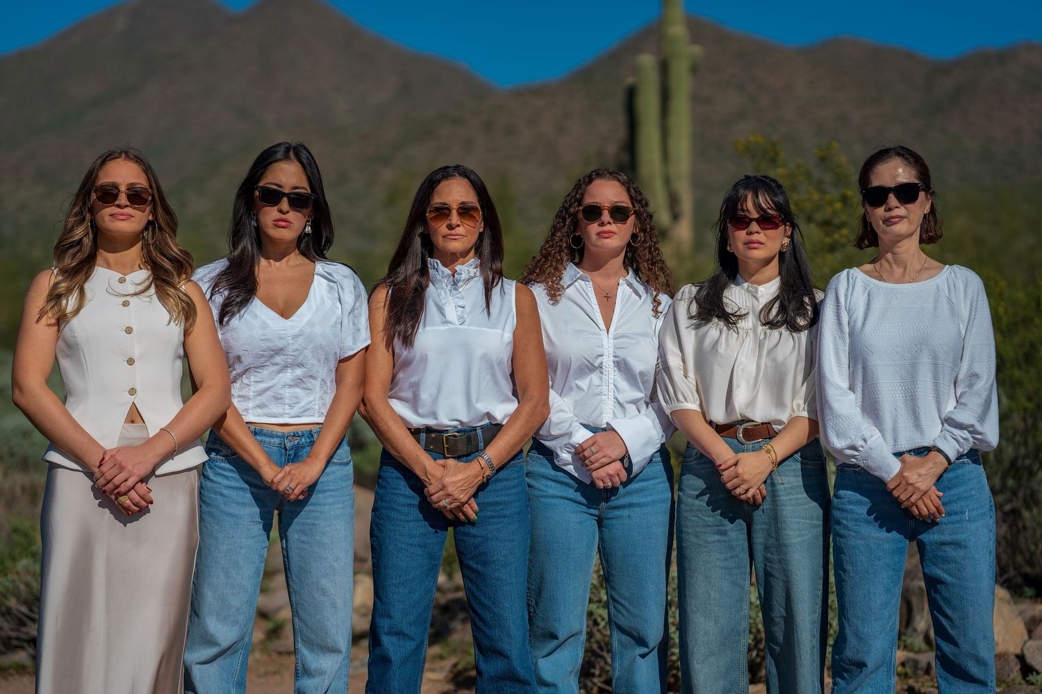 Six people in coordinated white tops and jeans pose together in front of desert mountains.
